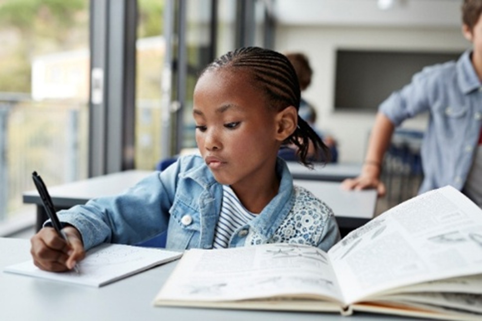 Young black student in classroom sitting at desk writing in notebook