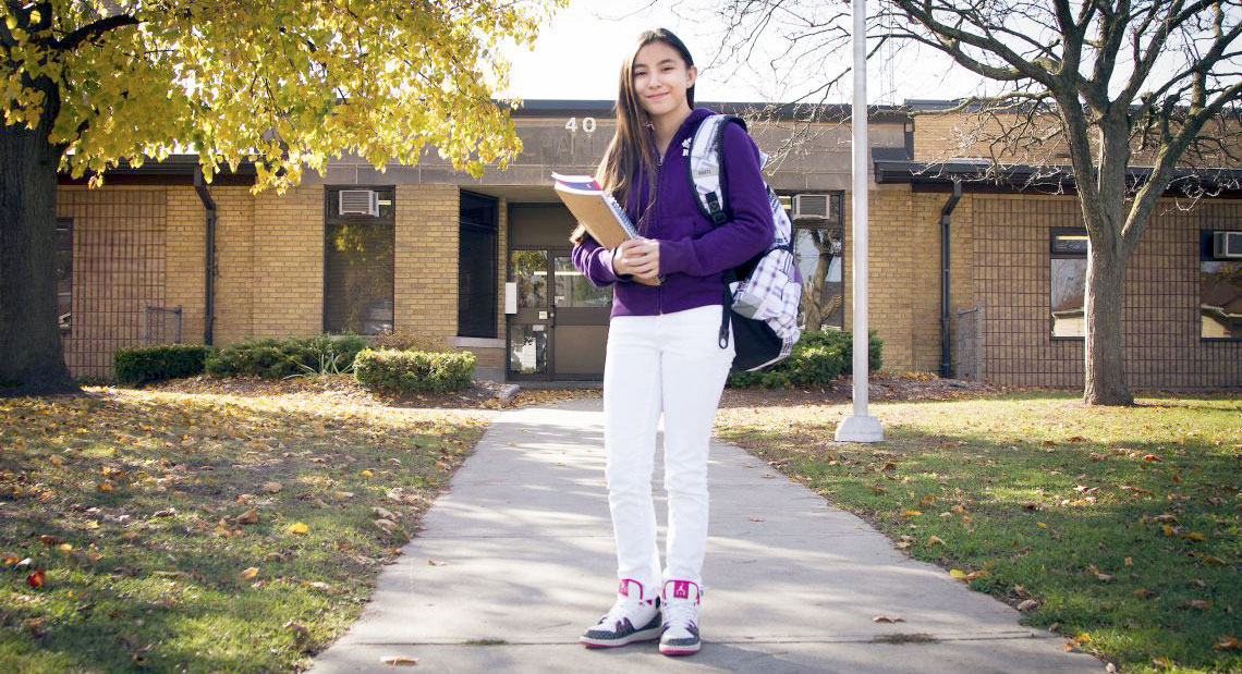 Child standing in from a school holding books